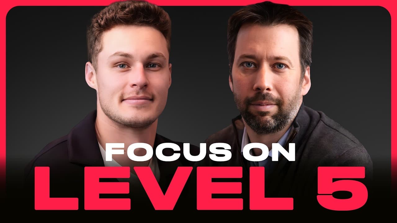 Joe Lonsdale speaking at a table with two other men, with a large screen displaying a city skyline behind them.